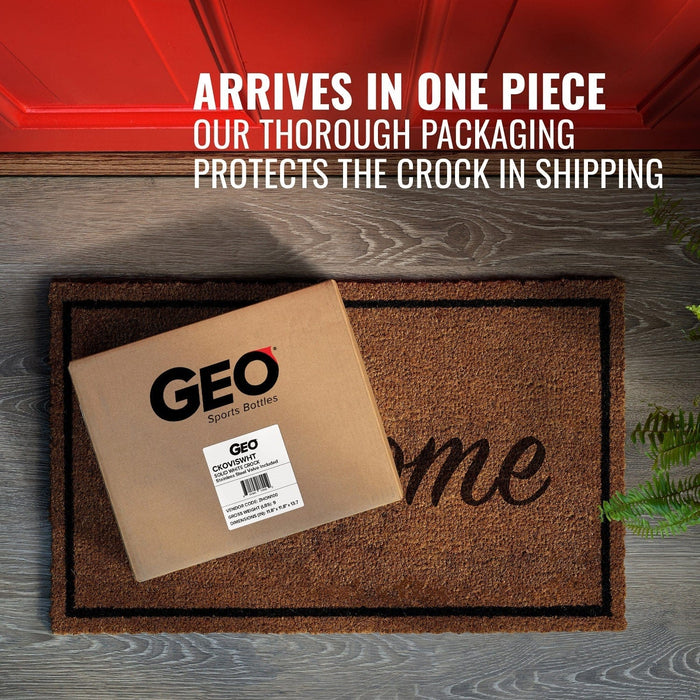 A cardboard box labeled GEO Porcelain Ceramic Crock Water Dispenser w/ Stand – Black sits on a brown doormat by a red door. Text above reads: ARRIVES IN ONE PIECE. OUR THOROUGH PACKAGING PROTECTS YOUR DISPENSER IN SHIPPING.