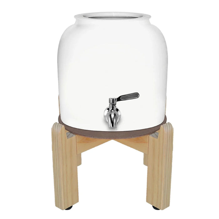 The GEO Porcelain Ceramic Crock Water Dispenser in white features a BPA-free ceramic body, a metal spigot, and sits securely on a four-legged wooden stand.