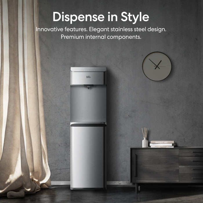 Stainless steel water dispenser against a gray wall with decorative elements.